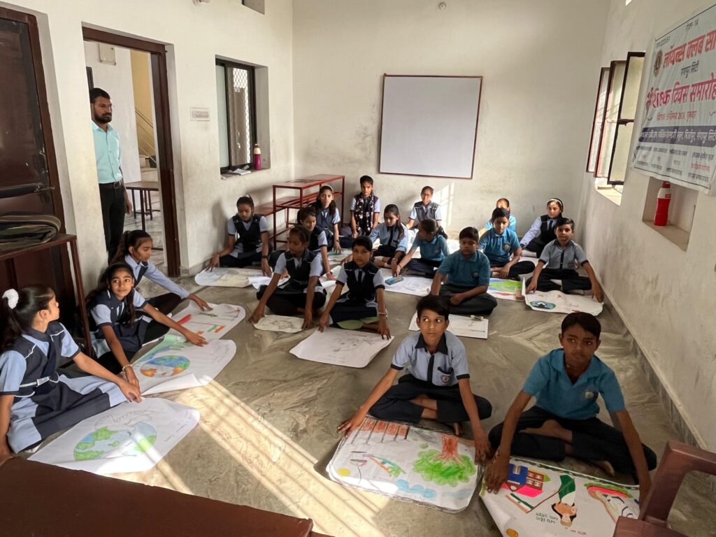 Students of MBM School Mirzapur participating in the Lions Club Sarthak Peace Poster Contest under Sevankur Seva Week, creating colorful artworks on the theme “We Are All One,” with judges and Lions members appreciating their creativity.